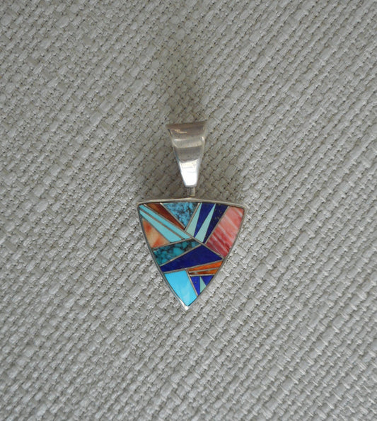 Triangle shaped pendant is made of turquoise , lapis, and spiny oyster stones with tiny pieces of silver between the pieces of stone. All set in Sterling Silver.  The reverse side has an intricate overlay design.  A large bail that spins.  Overall length is 1.5 inches.