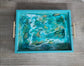 So stunning!  Multiple layers of resin give lots of depth to this tray.  Iridescent turquoise holographic film is layered with swirls of turquoise, white and gold.  The tray is a lightweight wood (MDF) and has matt gold handles for carrying.  Approximate size: 12 x 9 x 1.5 Inches   Care: Wipe with a clean damp cloth or alcohol wipe.  NOT for microwave or dishwasher.