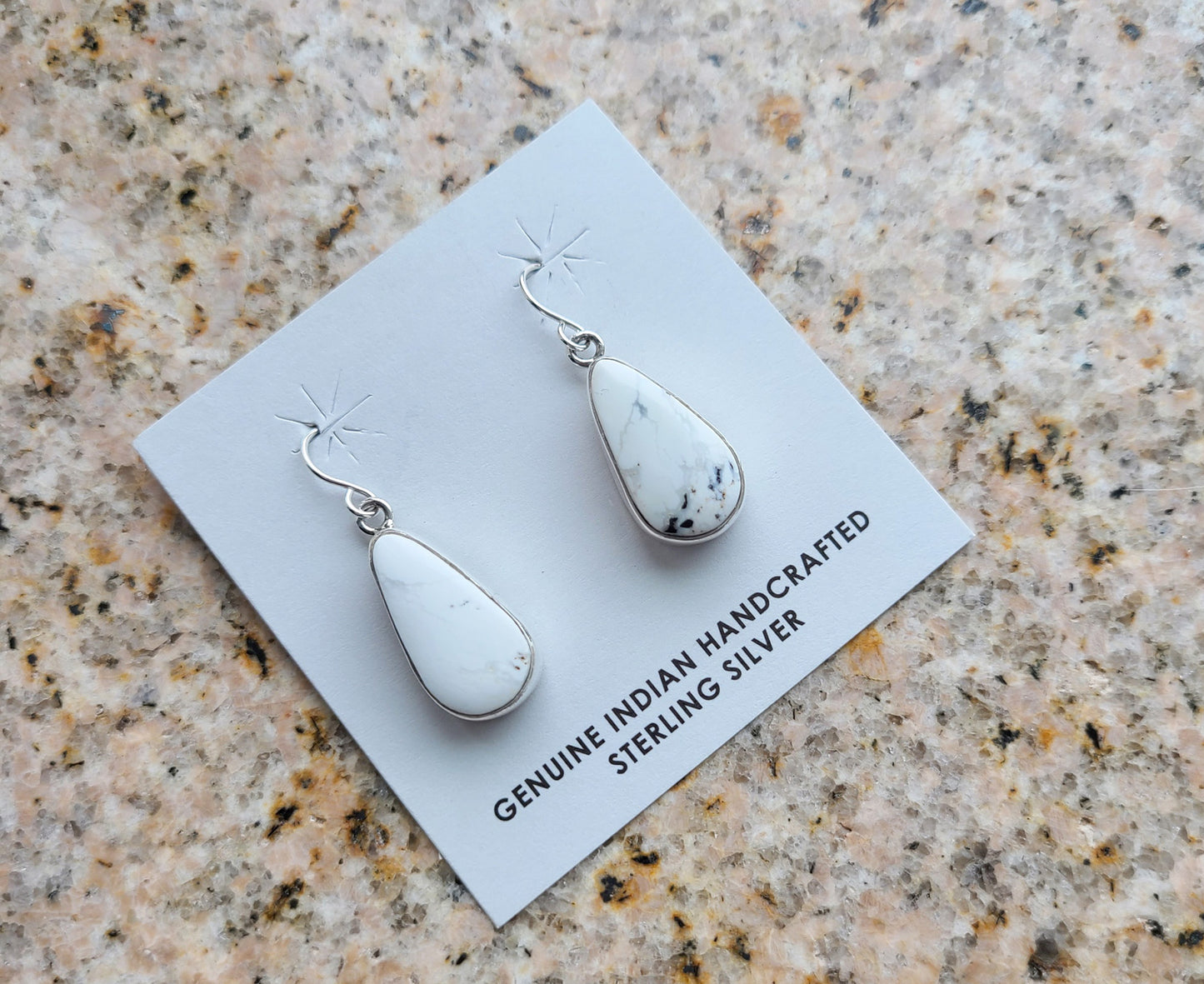 White Buffalo pear or teardrop shaped earrings set in a simple Sterling Silver plain bezel.  This White Buffalo is mostly white with a small amount of black matrix. On simple Sterling French Hooks. Navajo Artist, Shirley Henry. Approximately 1.25 inches long.